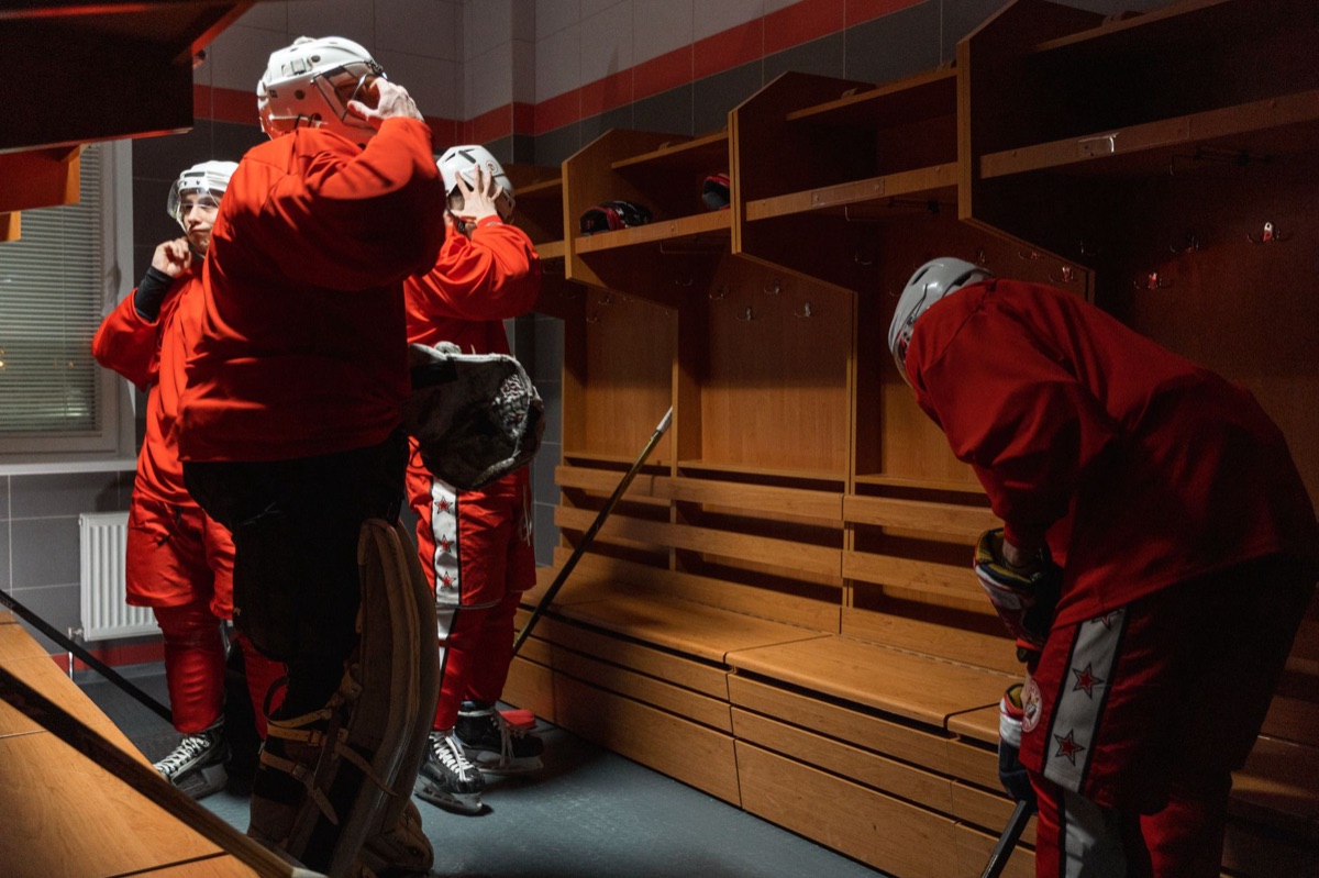 Hockey players in red uniforms preparing their gear in a locker room.