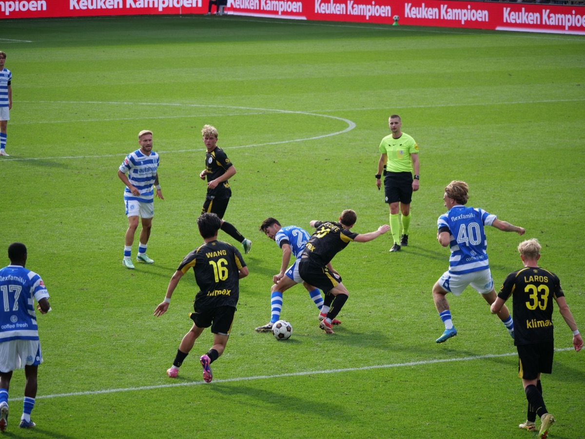 Soccer players in action during a competitive match under bright sunlight.