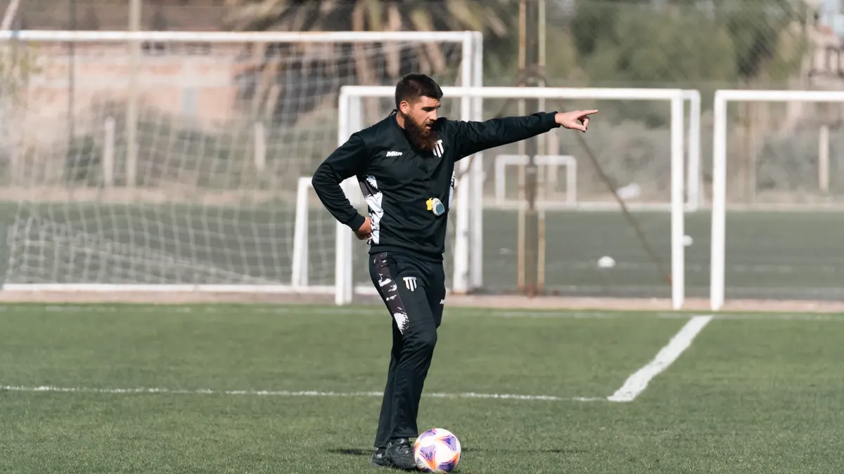A soccer coach giving instructions during a practice session on an outdoor field.
