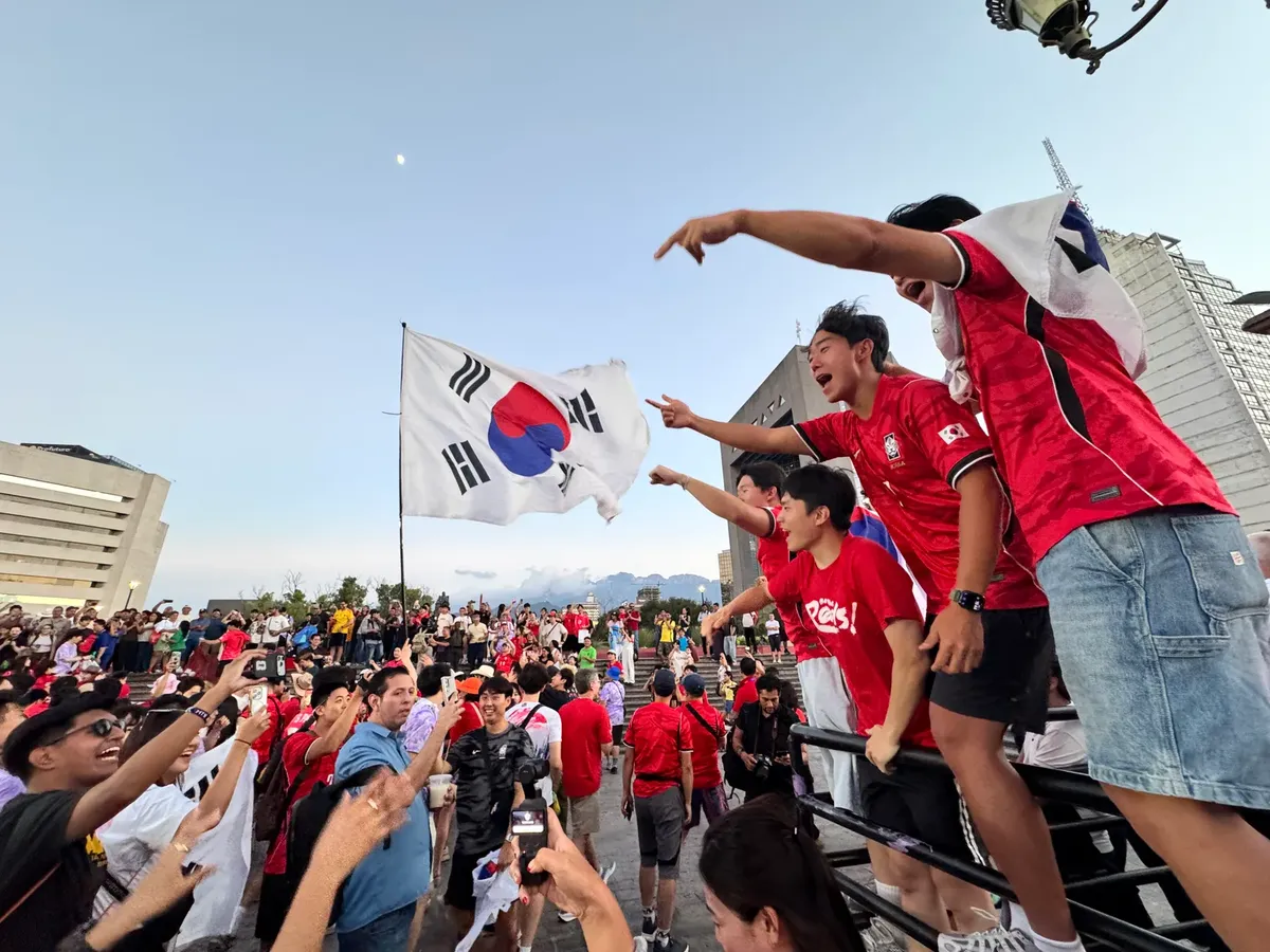 Energetic crowd celebrating outdoors with South Korean flag in vibrant city setting, capturing the thrill and unity.
