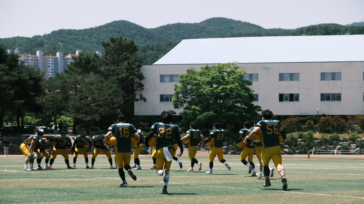 Football team in uniform practicing outdoors with mountains in background on a sunny day.